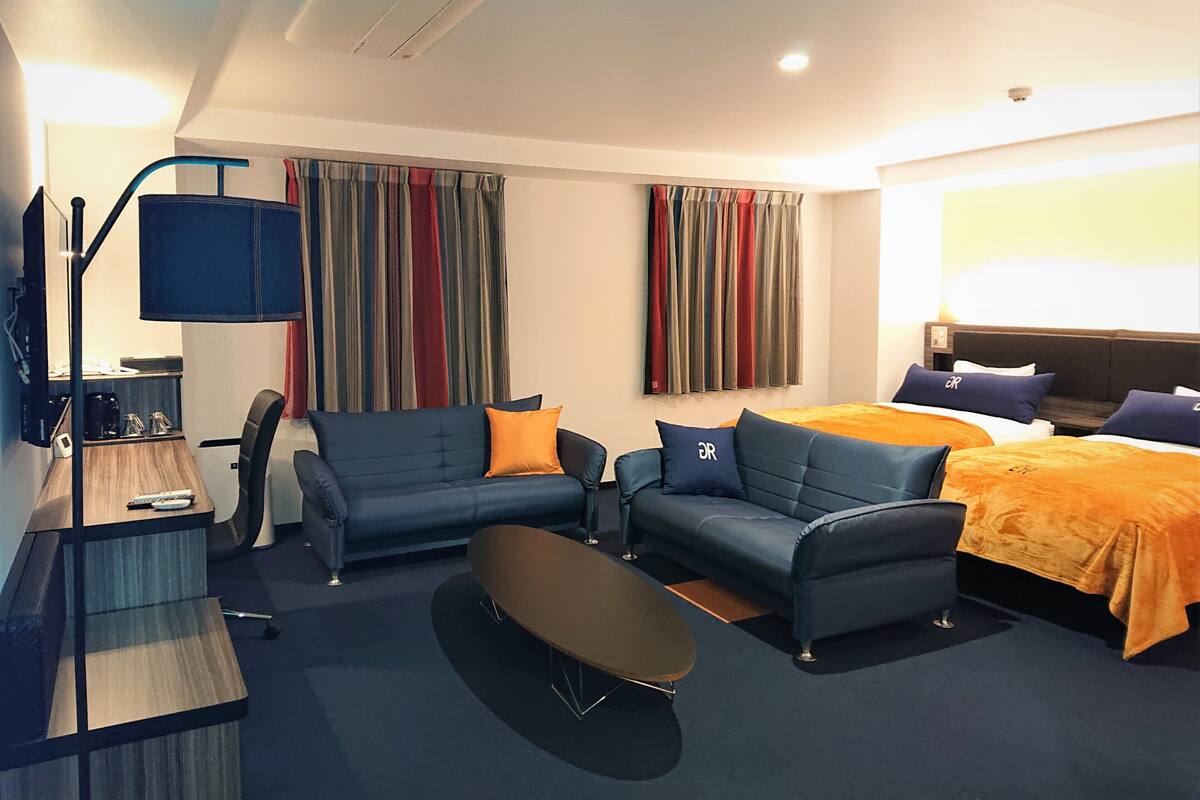 Ein modernes Hotelzimmer mit einer Couch, einem Couchtisch, einem Fernseher und einem Bett mit orangefarbener Bettwäsche.
