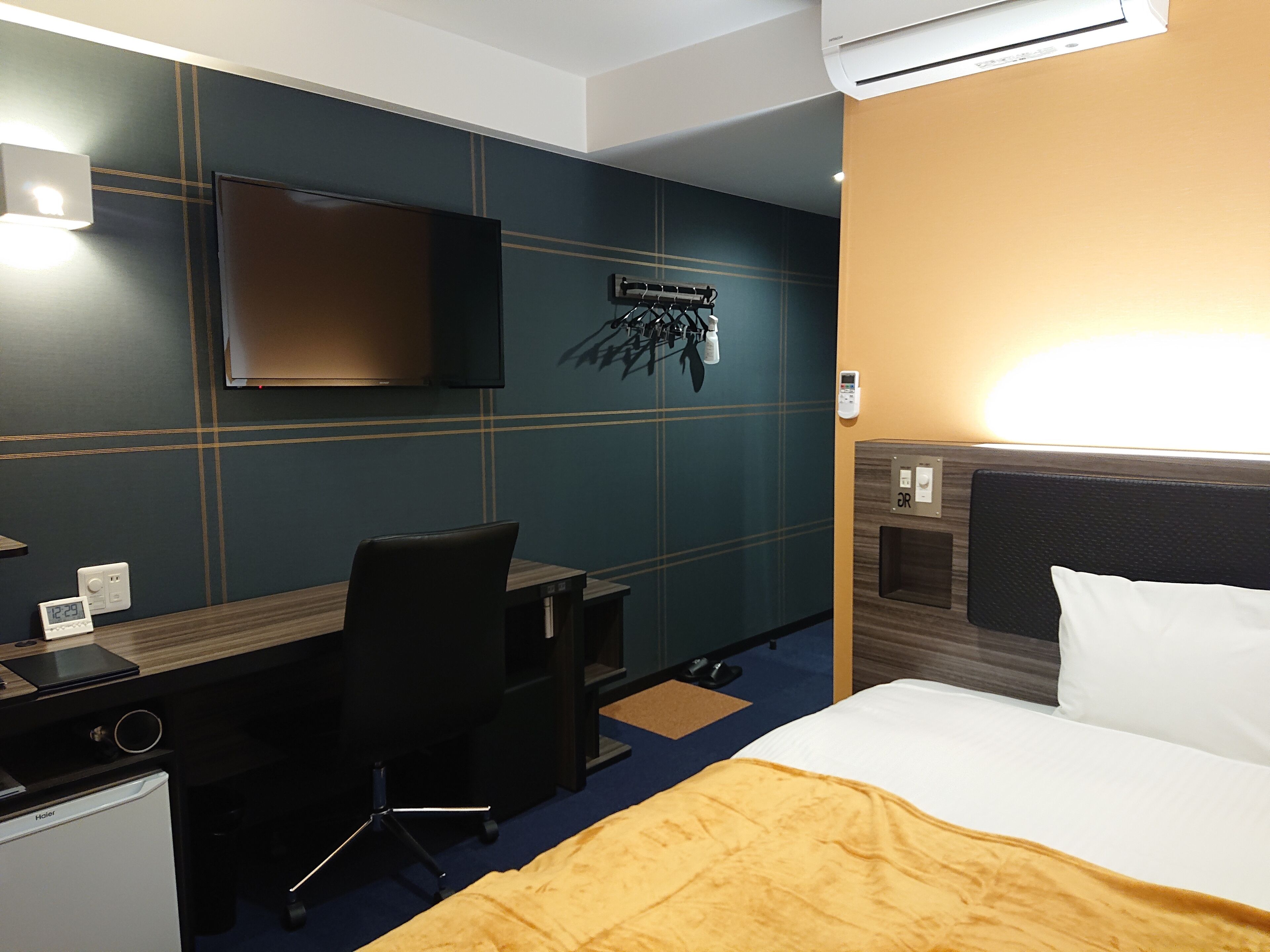 A hotel room with a bed, a desk, a chair, a television, and a wall-mounted air conditioning unit.