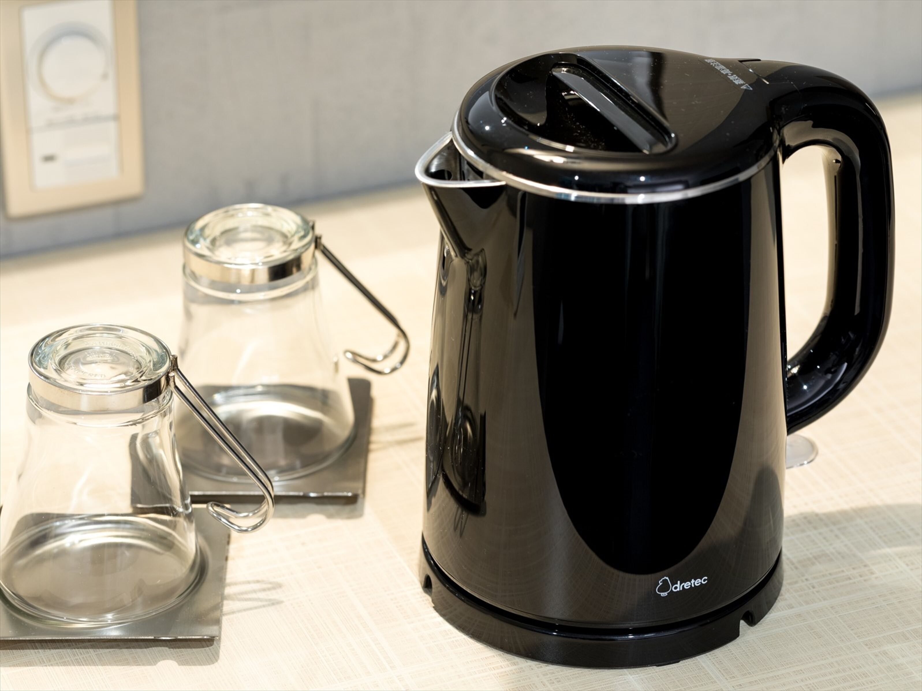 A black electric kettle with a handle, a glass carafe, and a glass teapot on a table.