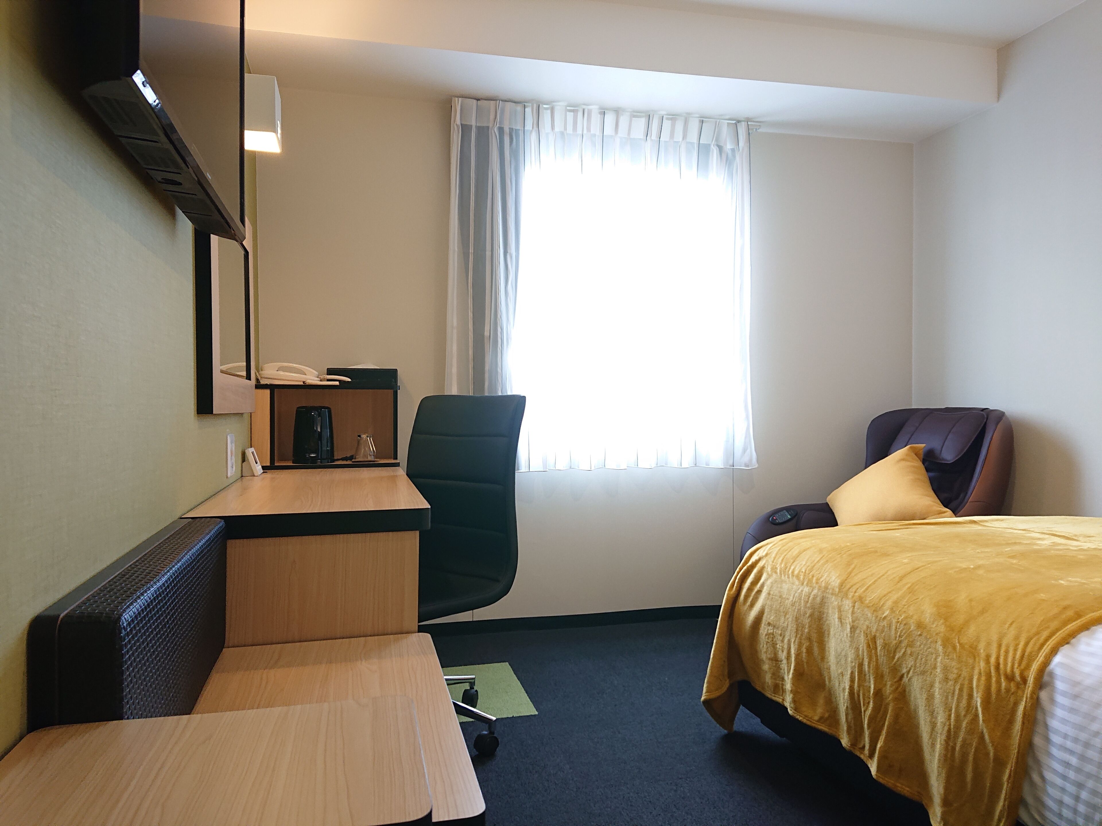 Habitación de hotel con escritorio, silla, cama y ventana con cortinas.