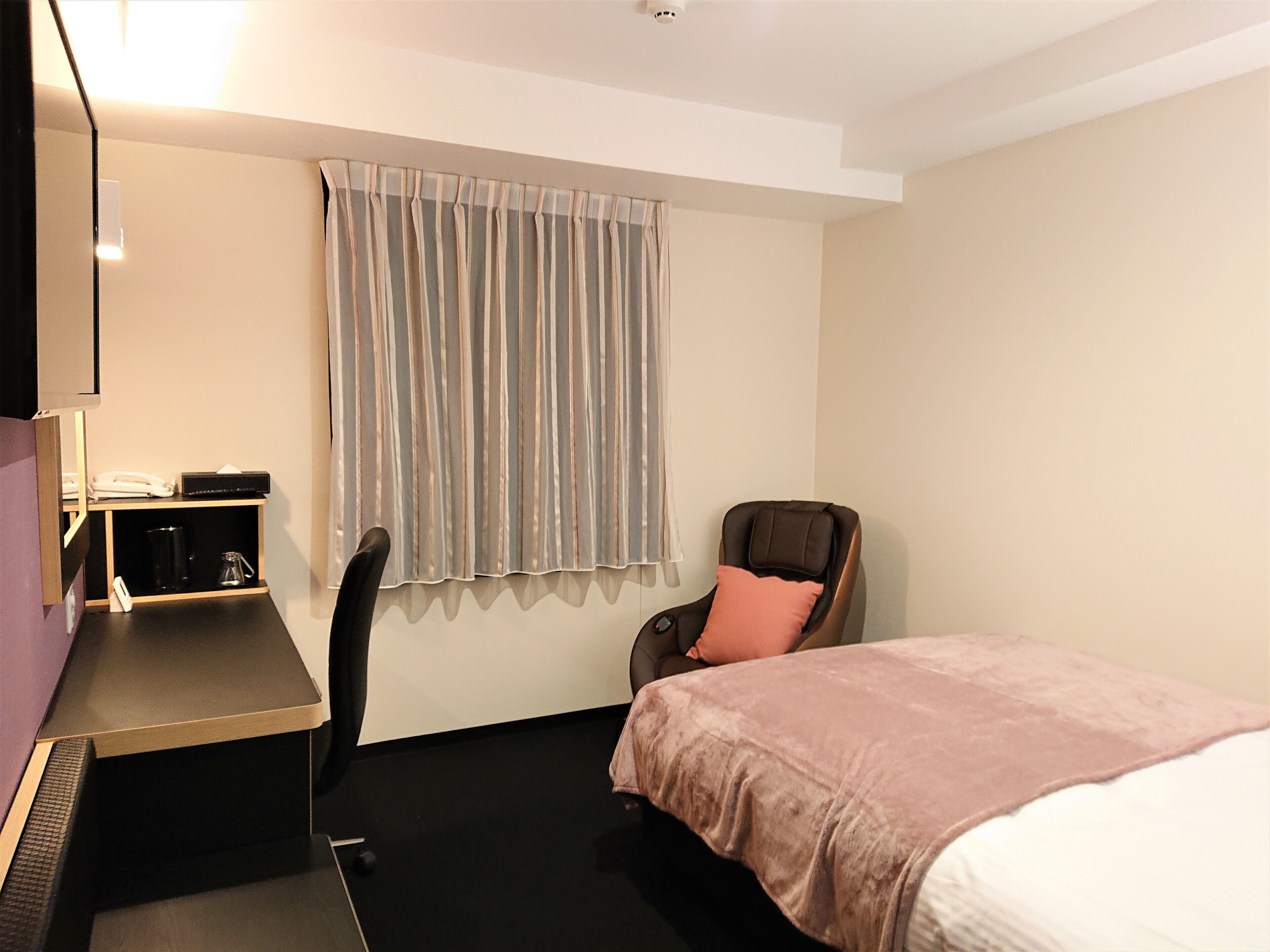 Een hotelkamer met een bed, een bureau, een stoel, een koffieapparaat en een raam met gordijnen.