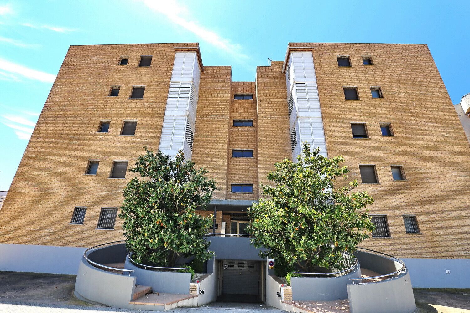 A multi-story building with a symmetrical facade, featuring a central entrance flanked by two large planters with trees.