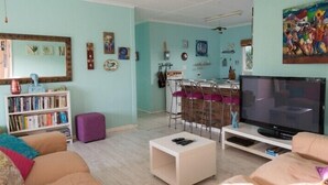 Ein Wohnzimmer mit Fernseher, Bücherregalen, einem Couchtisch und einem Essbereich mit Stühlen und Tisch.