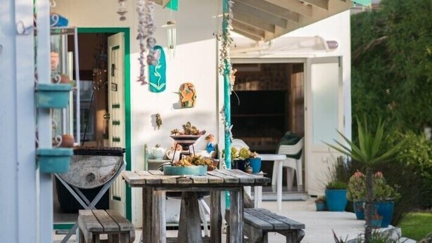 Eine Terrasse im Freien mit Holztisch und Stühlen, einem kleinen Grill und Topfpflanzen.