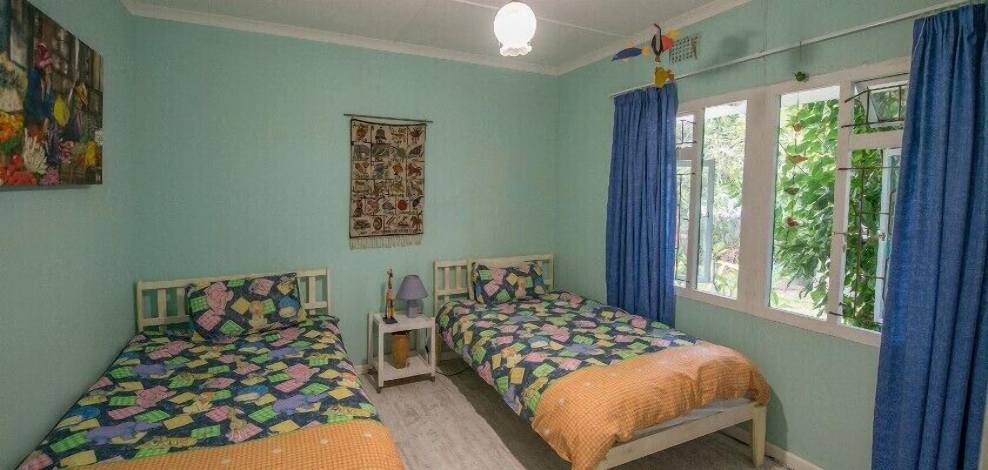 A room with two beds, a wall hanging, and a window with curtains.