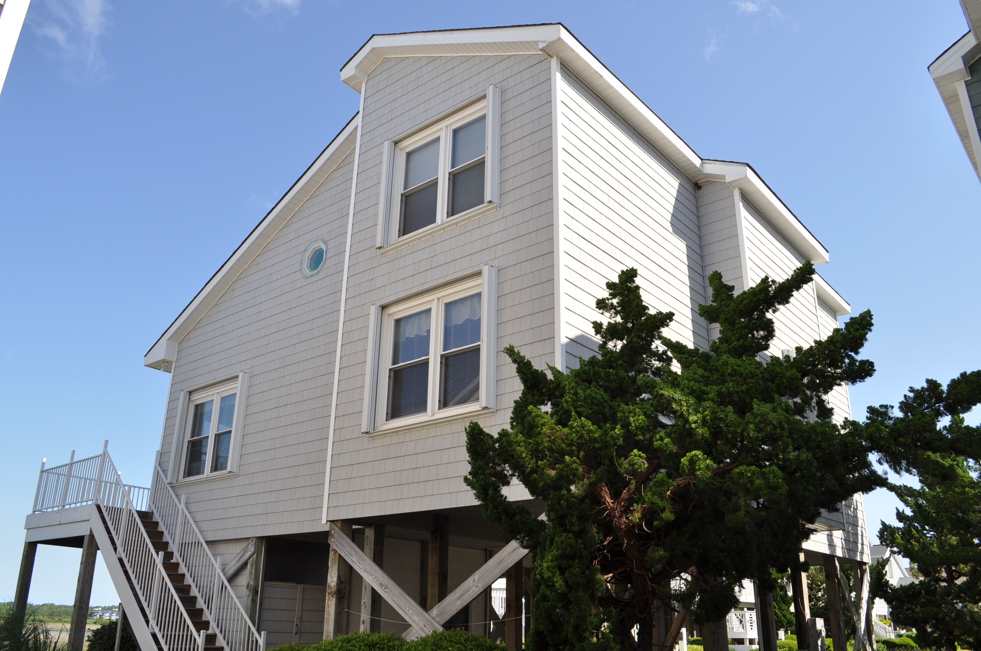 A two-story building with a white exterior, a staircase on the left, and a tree in the foreground.