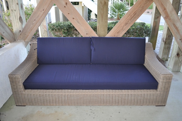 A wicker sofa with blue cushions, set against a backdrop of wooden beams and greenery.