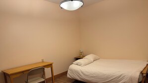 Une chambre à coucher avec un lit, un bureau, une chaise et une table de chevet avec une lampe.