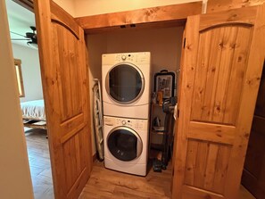 A laundry room with a stacked washer and dryer, wooden doors, and a ceiling fan.