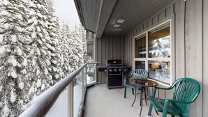 A balcony with a grill, two chairs, and a view of snow-covered trees. - Aspens #327 Prime Ski-in Ski-out Location! Pool, Hot tubs, Sleeps 8 (Whistler)