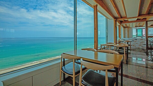 A restaurant with a view of the ocean, featuring wooden tables and chairs, large windows, and a modern interior design. - Yangyang Eight (Yangyang)