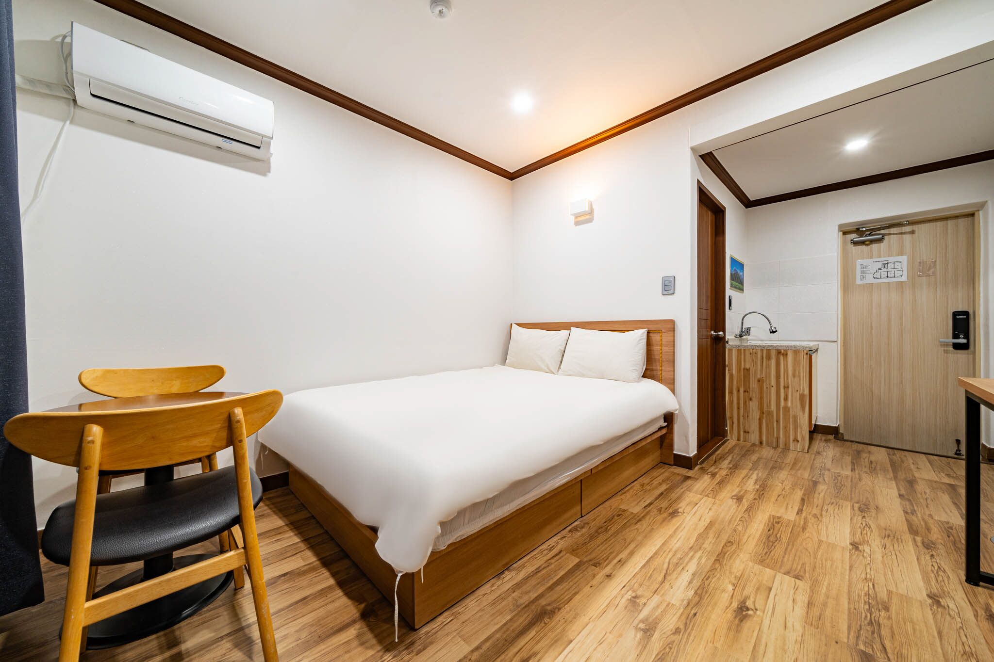 A room with a bed, a wooden chair, a small desk, and a wooden cabinet.