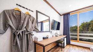 A hotel room with a wooden desk, a TV, a mirror, and a view of greenery through the window. - Yangyang Eight (Yangyang)