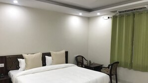 A neatly arranged hotel room with a large bed, a bedside table, a chair, and a desk with a chair. - Hotel Himalayan (Dehradun)