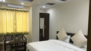 A hotel room with a bed, a desk, two chairs, a mirror, and an air conditioning unit. - Hotel Himalayan (Dehradun)