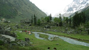 A mountainous landscape with a river, grazing animals, and a small building with a red roof. - Hotel Himalayan (Dehradun)