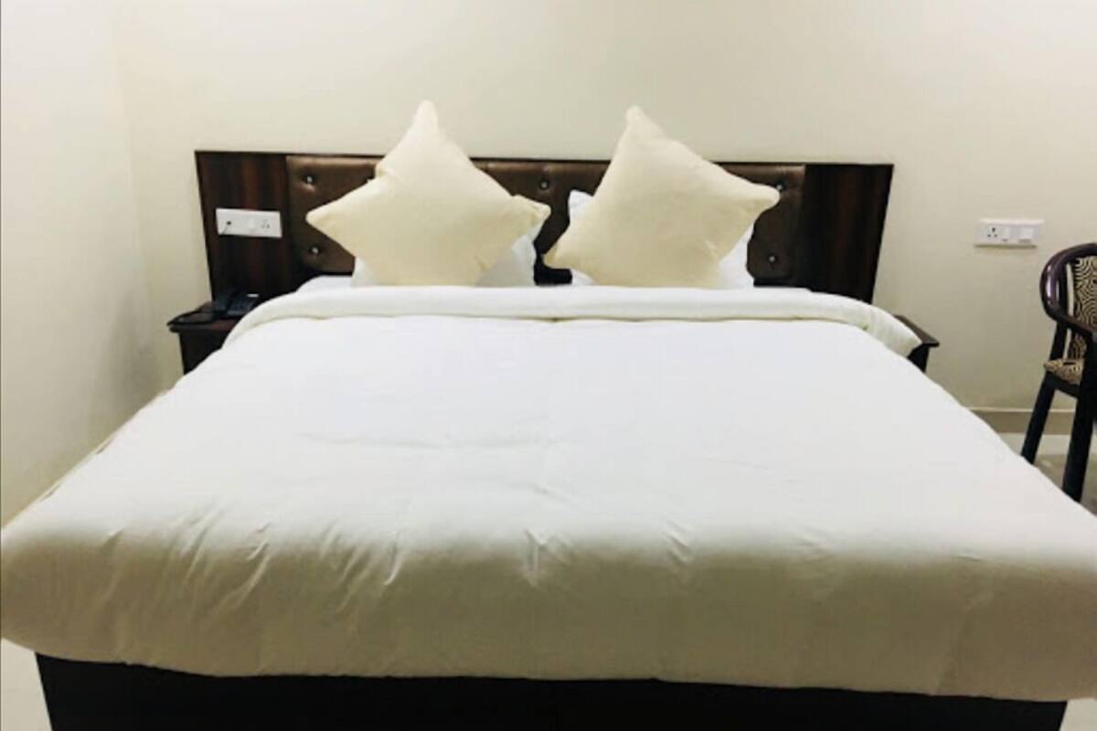 A neatly made bed with a headboard, two pillows, and a bedside table with a phone.