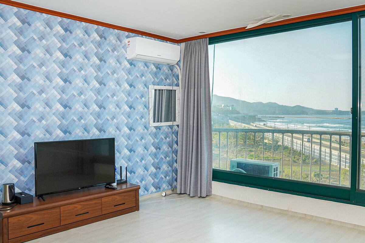 A room with a large window, a flat-screen TV, and a wooden cabinet.