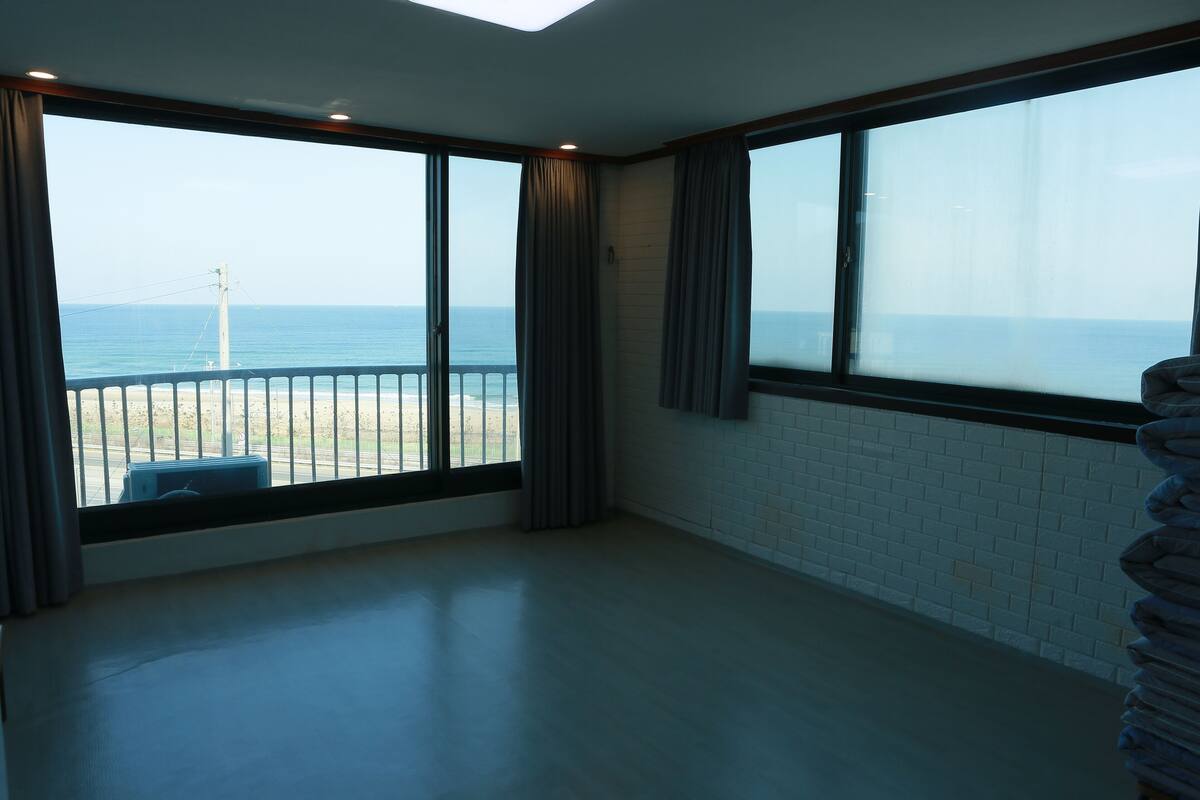 A room with large windows offering a view of the sea and a distant power line structure.