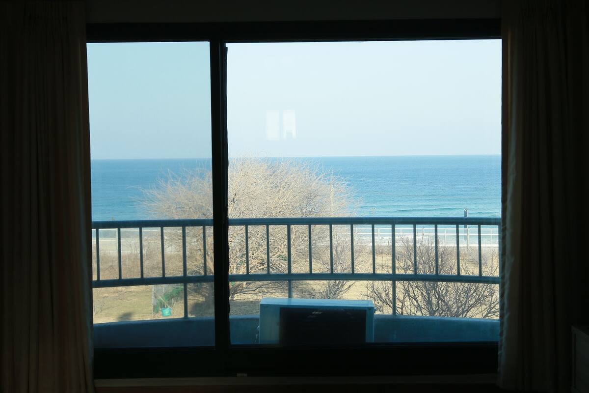 A room with a large window overlooking a beach and ocean.