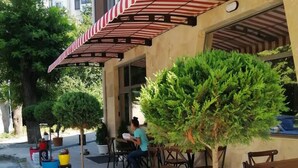 An outdoor cafe with tables and chairs, potted plants, and a striped awning. - The Old Bakery Apartments (Plovdiv)