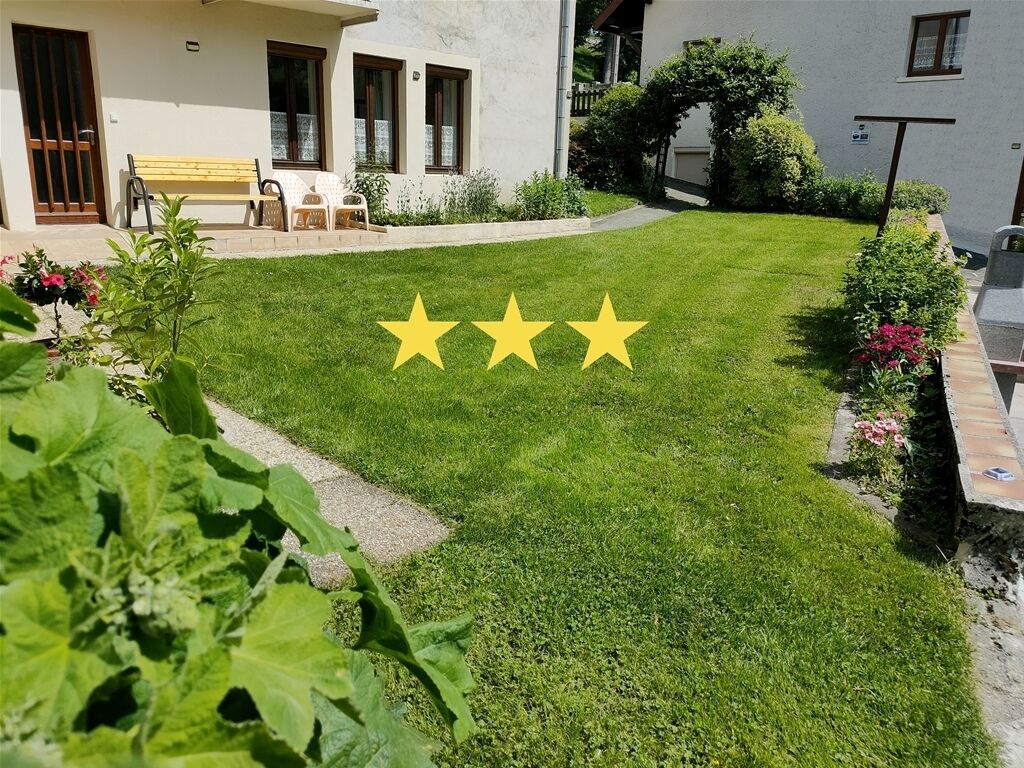 Un césped cuidado con tres estrellas amarillas, un banco y un camino que lleva a un edificio con ventanas y una puerta.