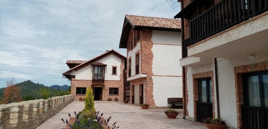 A two-story house with a balcony, stone wall, and potted plants.