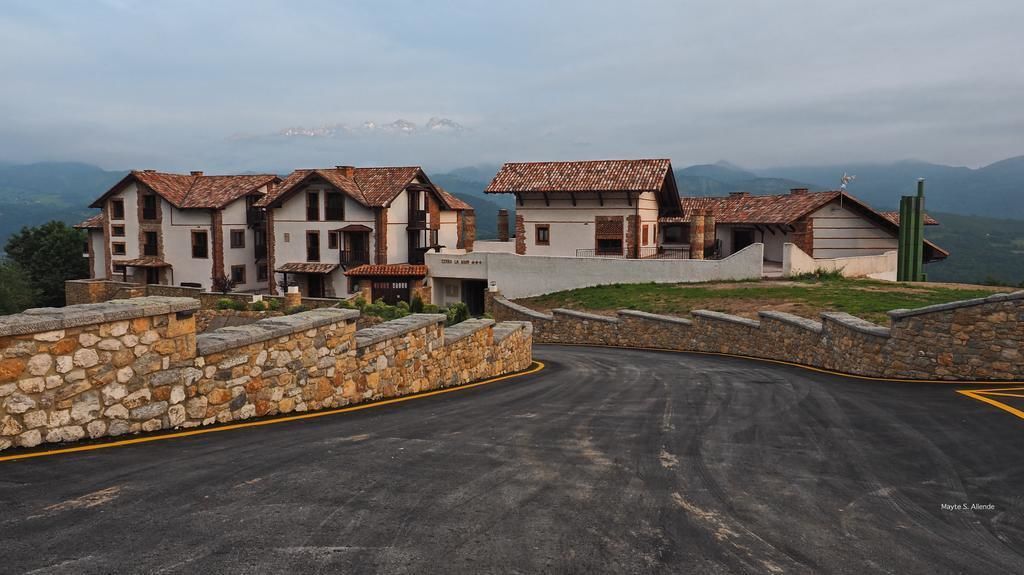 Un edificio de paredes de piedra con un camino pavimentado que lo lleva a la entrada, al pie de montañas.