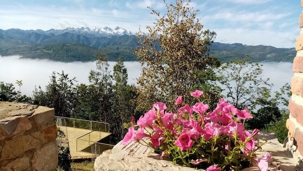 A stone structure with pink flowers in the foreground, overlooking a lake and mountains. - Hotel Cerro la Nina (Cangas de Onis)