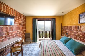 Une chambre avec un lit, un bureau et un téléviseur fixé au mur en briques.
