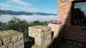 A stone wall with a brick building, a stone ledge, and a view of mountains and clouds. - Hotel Cerro la Nina (Cangas de Onis)