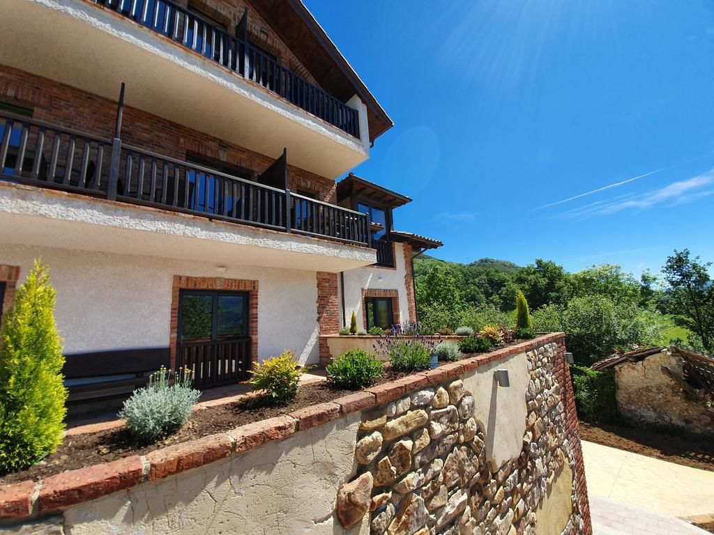 Un edificio de varios pisos con balcones, un muro de piedra y un jardín ajardinado.