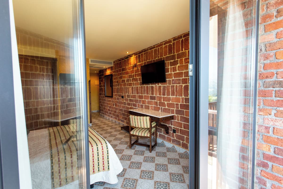 Une pièce avec un mur en briques, un téléviseur à écran plat fixé au mur, une table en bois et une couvre-lit à motifs.