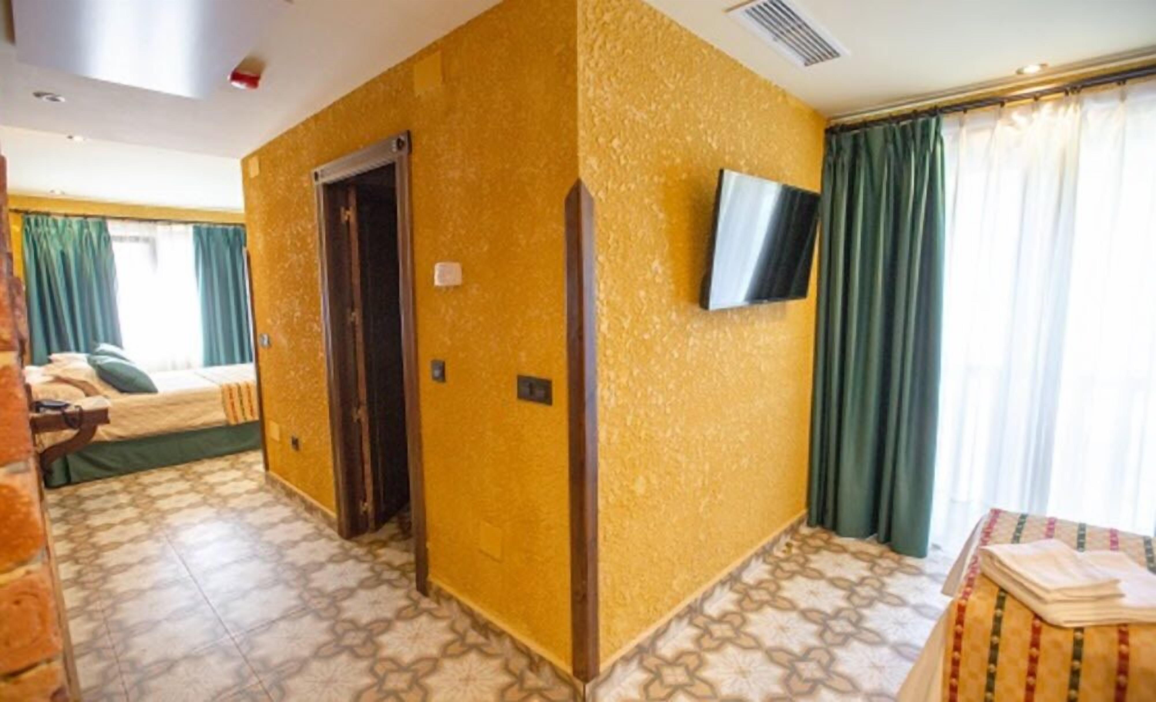 Una habitación de hotel con piso estampado, cama con ropa de cama verde, televisor montado en la pared y puerta con picaporte.