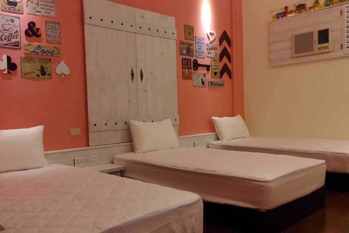 A room with three single beds, a white wardrobe, and a wall decorated with various coffee-related signs.