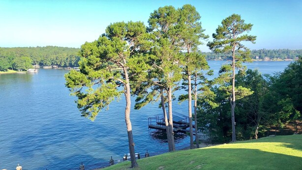 Blick auf einen See mit einer Rasenfläche, einem Steg und blauem Himmel.