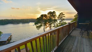 Eine Holzterrasse mit Blick auf einen See und Bäume bei Sonnenuntergang.