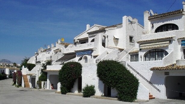 Fila de edificios blancos con ventanas arqueadas y balcones, cielo despejado y una calle en primer plano.