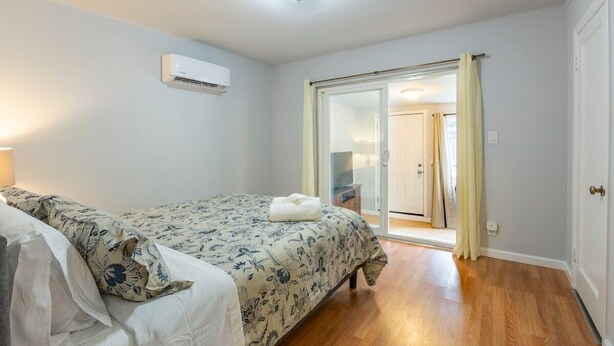 Un dormitorio con cama, ventana, equipo de aire acondicionado y puerta que da a otra habitación.