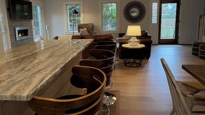 A spacious kitchen with a long island, bar stools, a dining area with a table and chairs, and a fireplace. - Modern 5 Bedroom Home. Newly constructed. Large yard. Close to beaches and town. (Nantucket)