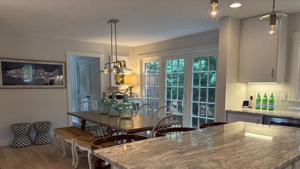 A modern kitchen with a large island, white cabinetry, and a dining area with a wooden table and chairs. - Modern 5 Bedroom Home. Newly constructed. Large yard. Close to beaches and town. (Nantucket)
