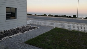 Una casa moderna con camino de entrada pavimentado, cerca blanca en forma de espiga y vista al océano al atardecer.