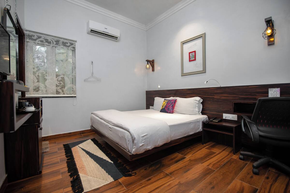 Un dormitorio ordenado con cama, mesita de noche, silla y escritorio con lámpara.