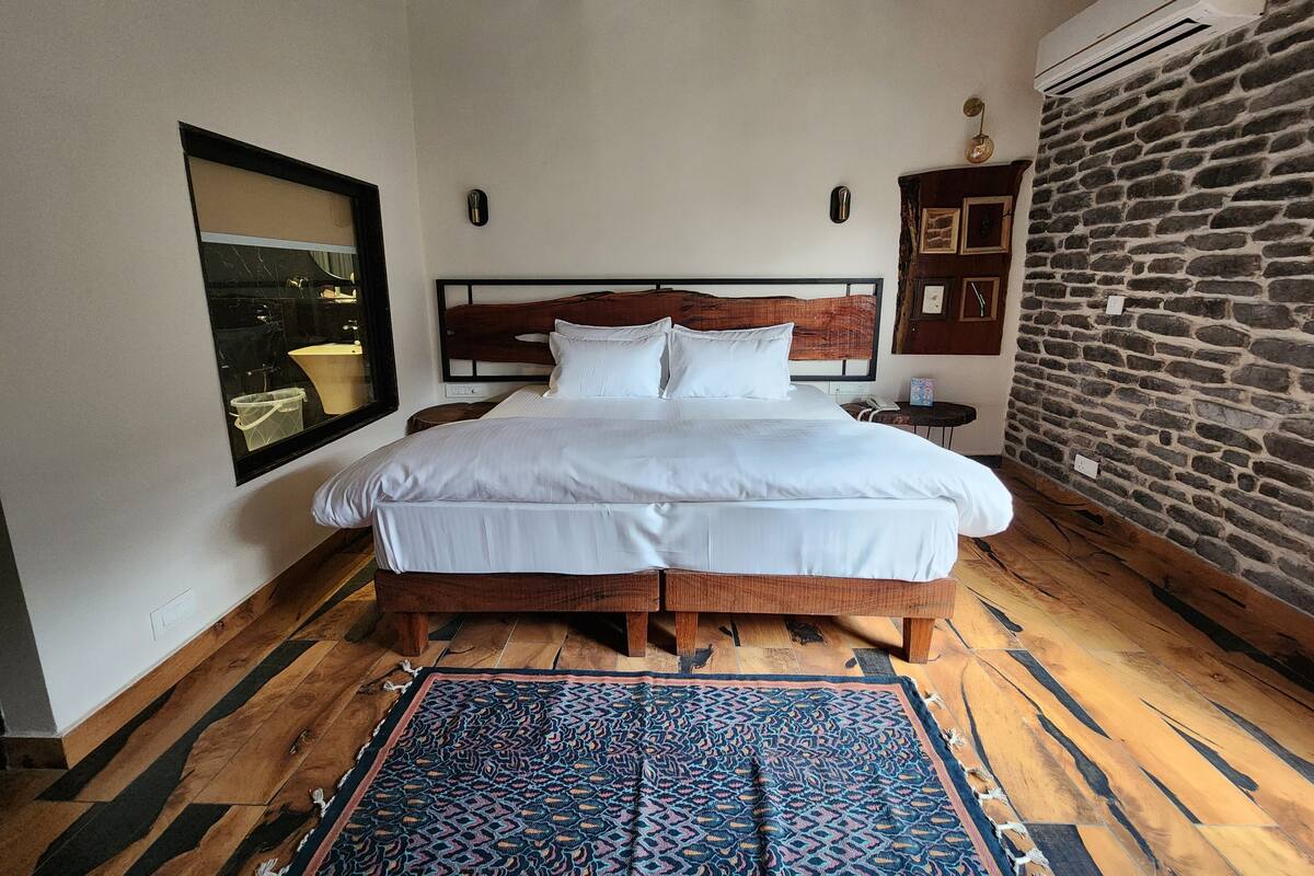 Un dormitorio bien iluminado con una cama grande, cabecera de madera, alfombra estampada y pared de piedra.