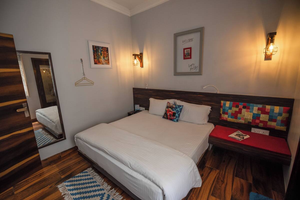 Un dormitorio ordenado con una cama grande, una mesita de noche, una lámpara colgante y un letrero de bienvenida.