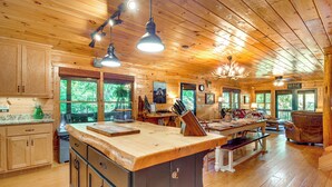 Un'ampia baita di legno con una grande cucina, un tavolo da pranzo e numerose finestre che offrono vista sulla foresta circostante.