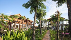 Um caminho bordeado por plantas tropicais que leva a um edifício com telhado tradicional.