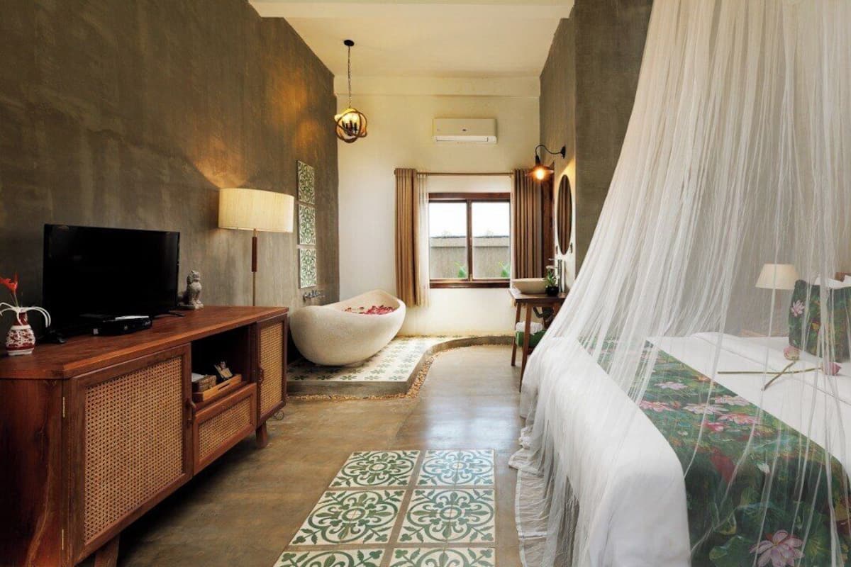A bedroom with a bed, a television, a sofa, and a window.