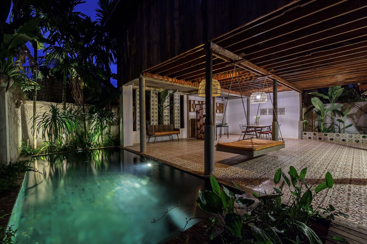A covered outdoor area with a pool, wooden furniture, and potted plants.