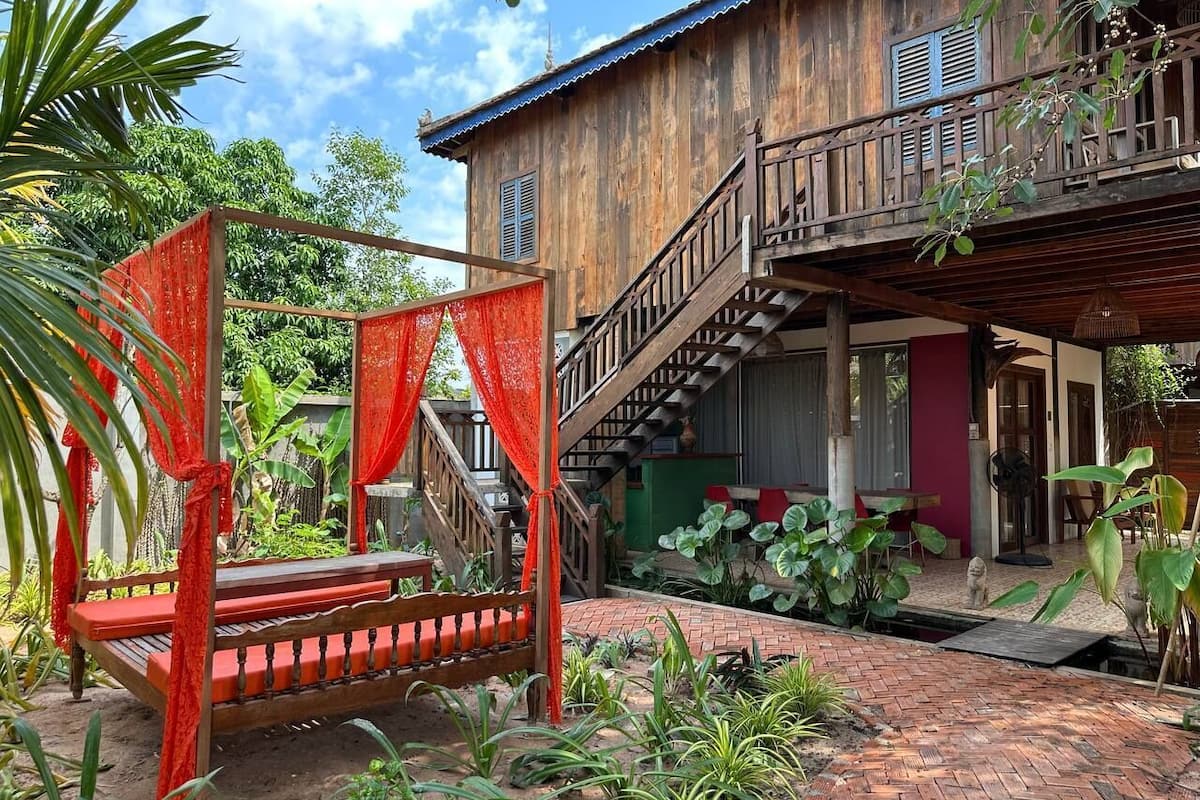 A wooden house with a balcony, a staircase, and a garden with plants.